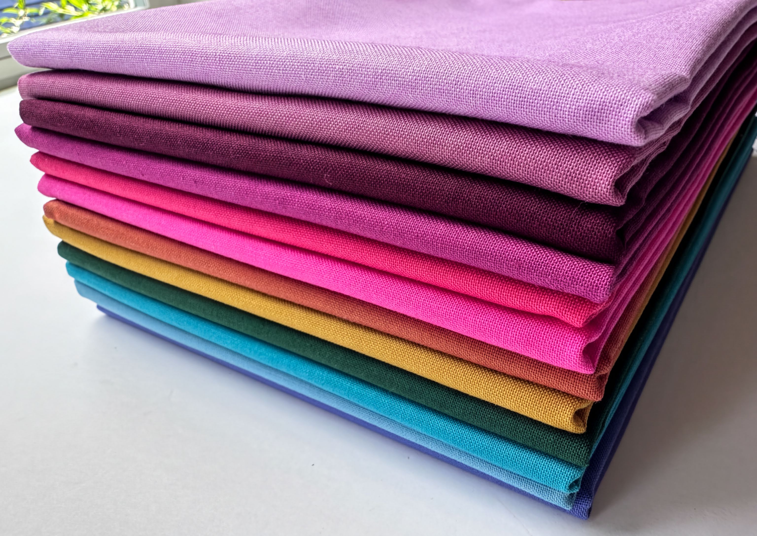 A stack of colorful fabric swatches in various shades of purple, pink, orange, yellow, green, blue, and purple.