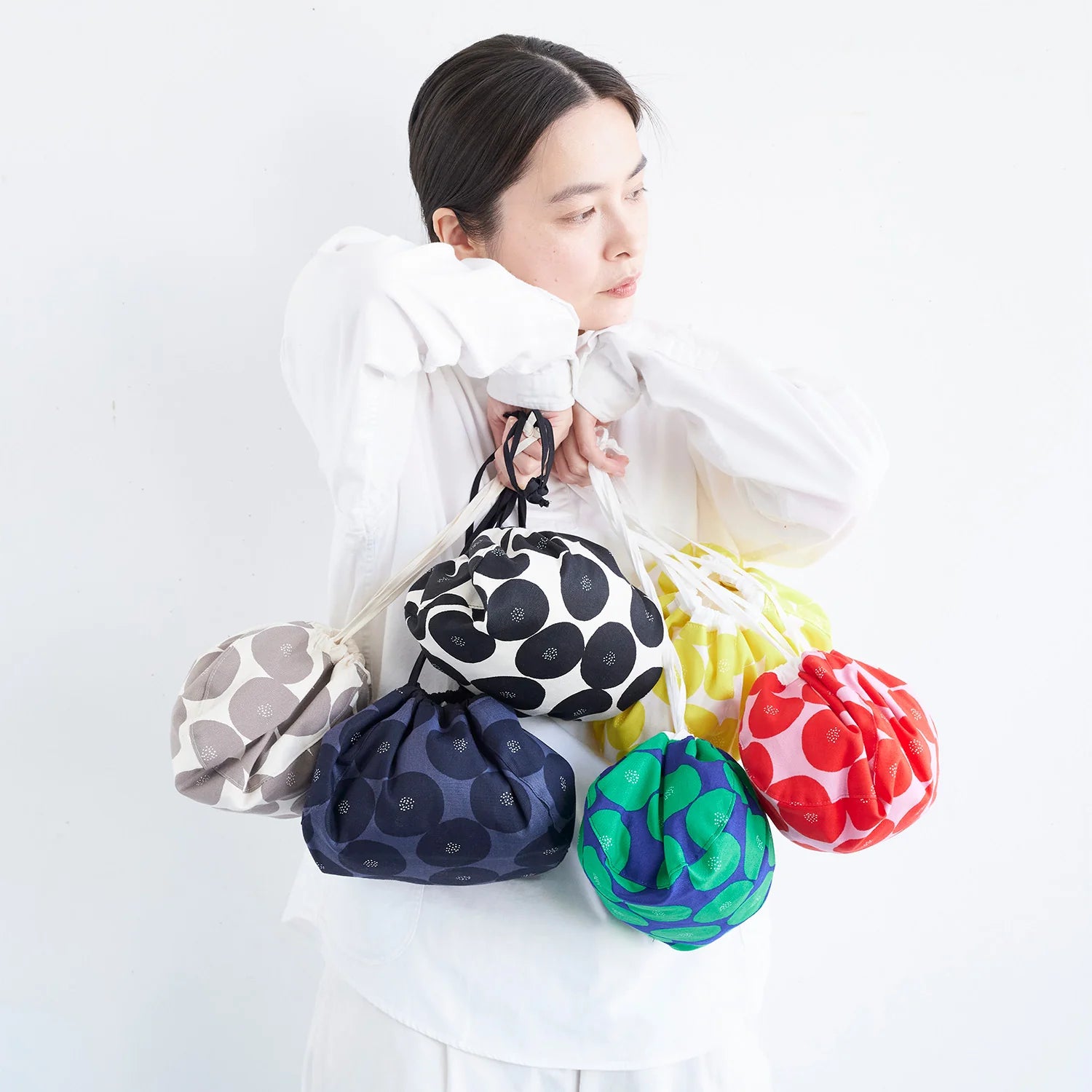 A woman in a white shirt is holding a variety of colorful bags, including polka dot, black and white, yellow, red, and green bags.