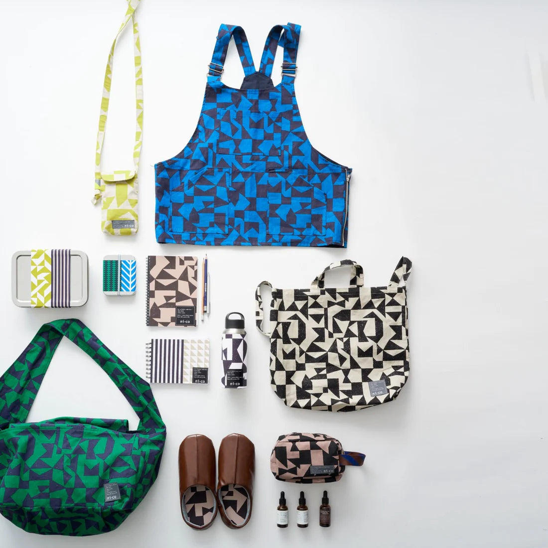 a variety of colorful and patterned bags and accessories, including a blue and black patterned apron, a green and black bag, a black and white patterned bag, and a black and white bag with a geometric pattern.