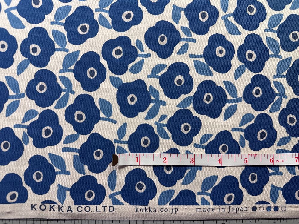 a fabric with a repeating pattern of blue flowers on a white background. A ruler is placed next to the fabric, indicating the size of the fabric.