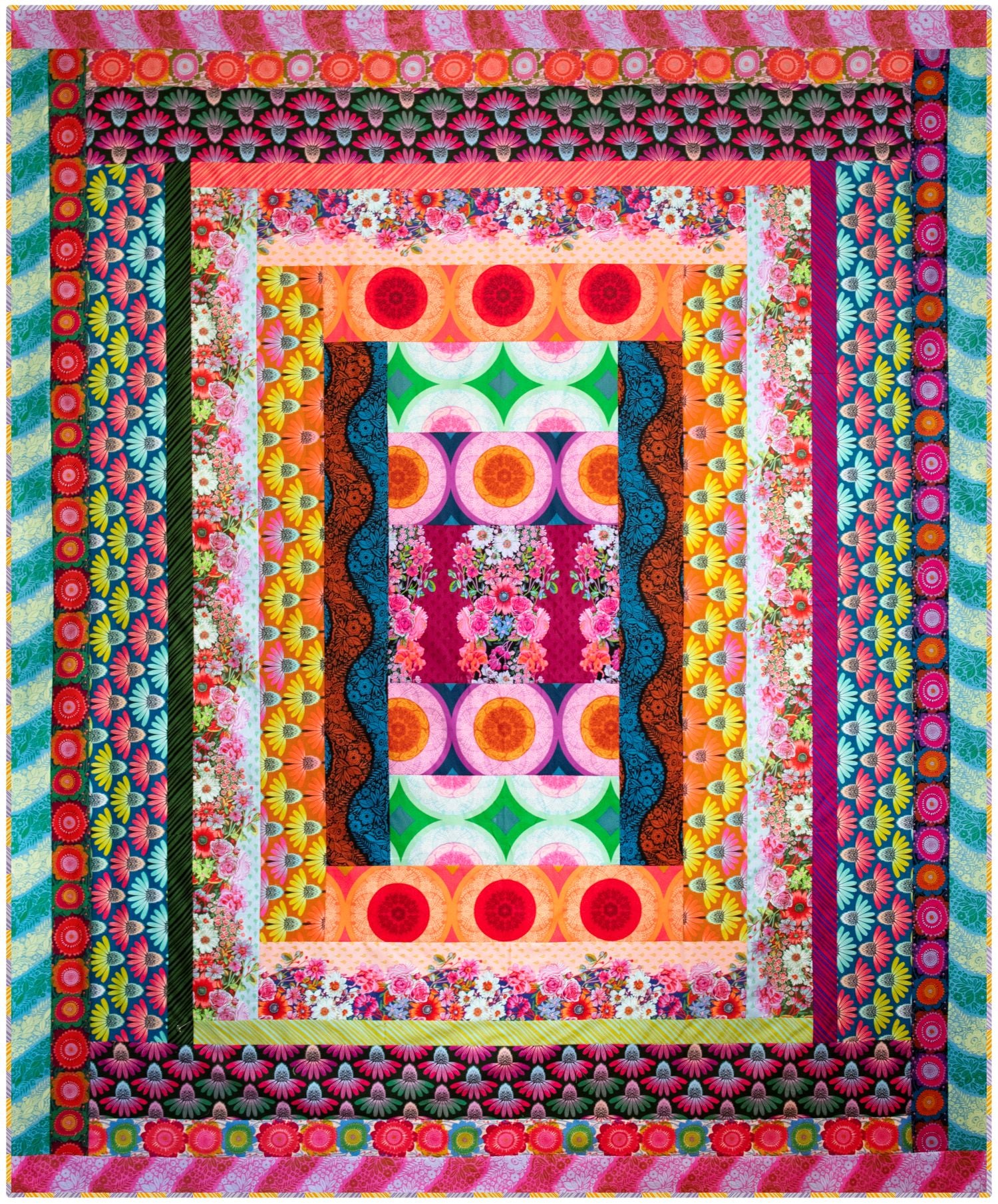 The image is a vibrant and colorful quilt with a repeating pattern of flowers and geometric shapes in various shades of pink, orange, green, and blue.