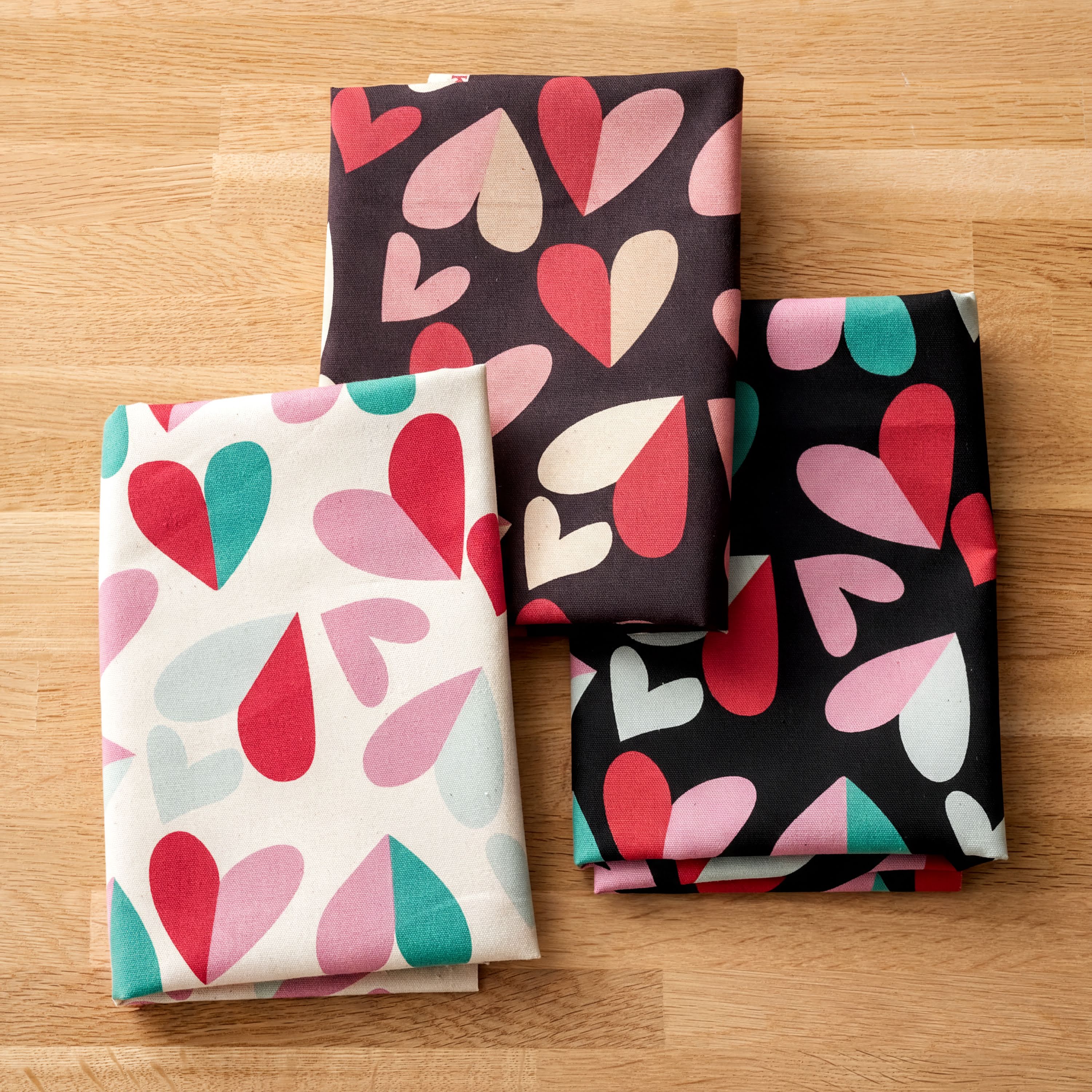 four folded fabric pieces with different heart patterns on them, laid out on a wooden surface.