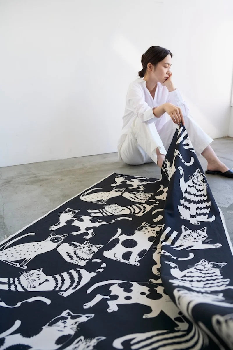 A woman sits on the floor, holding a large black and white fabric with a cat pattern.