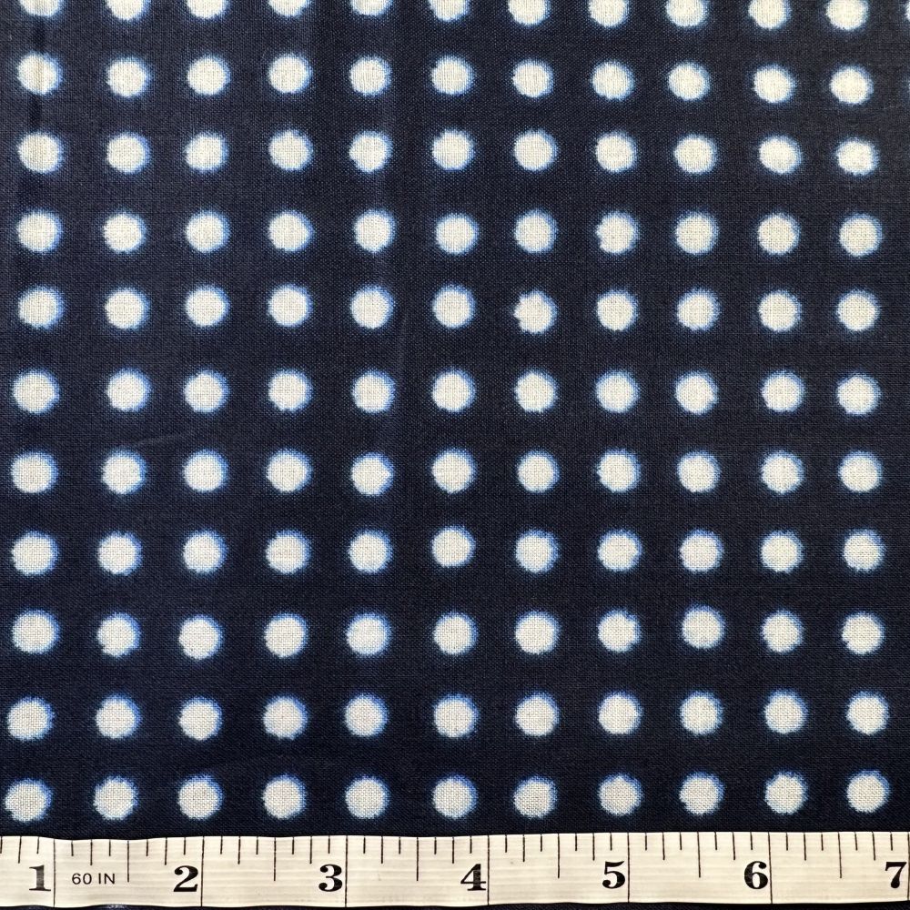 a close-up view of a fabric with a repeating pattern of white dots against a dark background. The fabric appears to be a dark-colored material with a polka dot pattern. A ruler is visible at the bottom of the image, indicating the size of the fabric.
