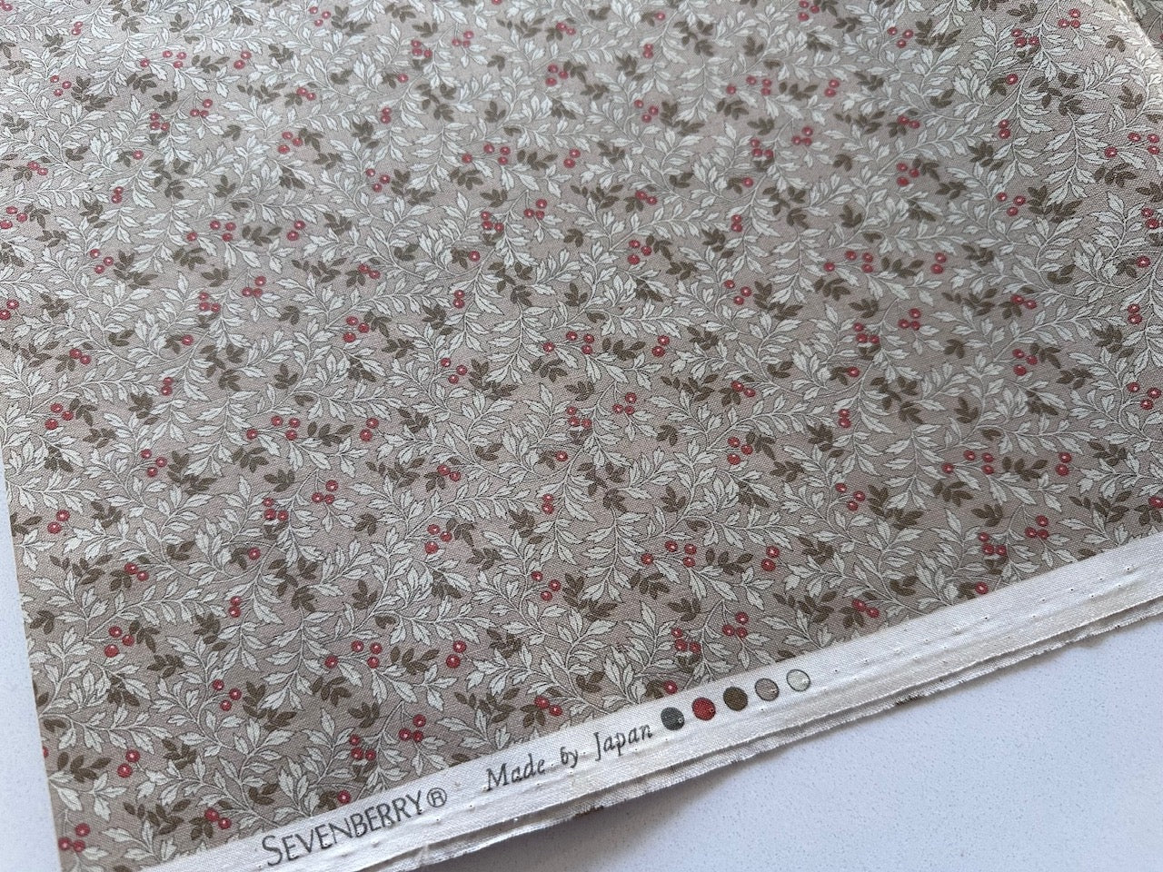 a close-up view of a fabric with a floral pattern, featuring small red berries scattered throughout the design.
