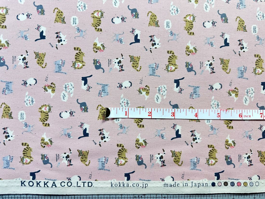 a fabric with a repeating pattern of cats in various colors and sizes, along with a ruler for scale.