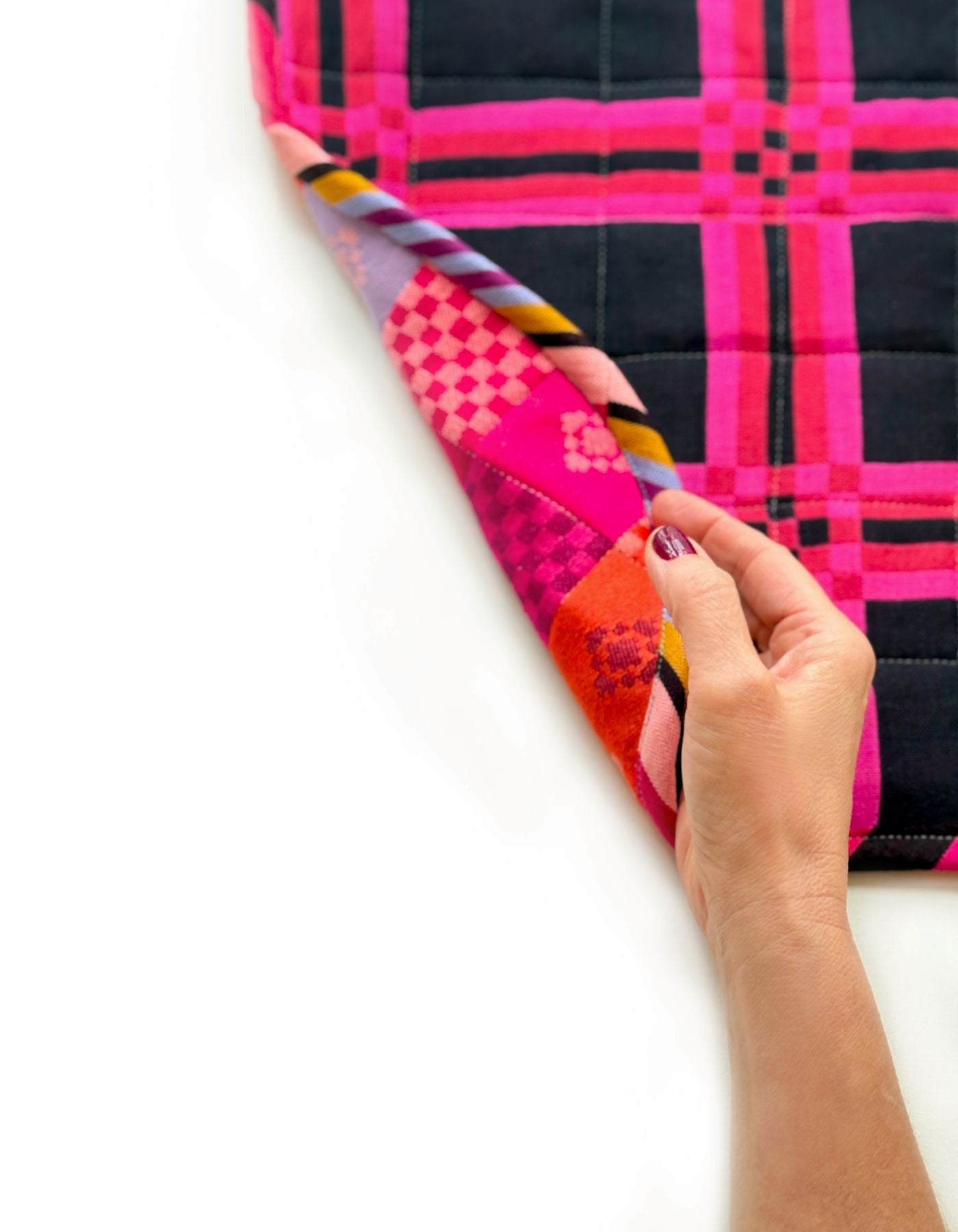 A hand is holding a colorful, patterned fabric with a pink and black checkered design, which appears to be a quilt or textile.