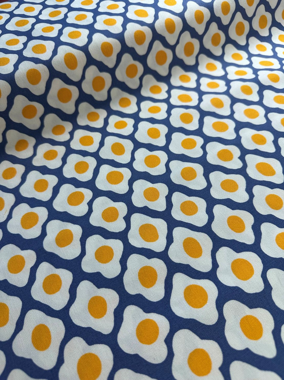 a close-up view of a fabric with a repeating pattern of yellow and white egg shapes.