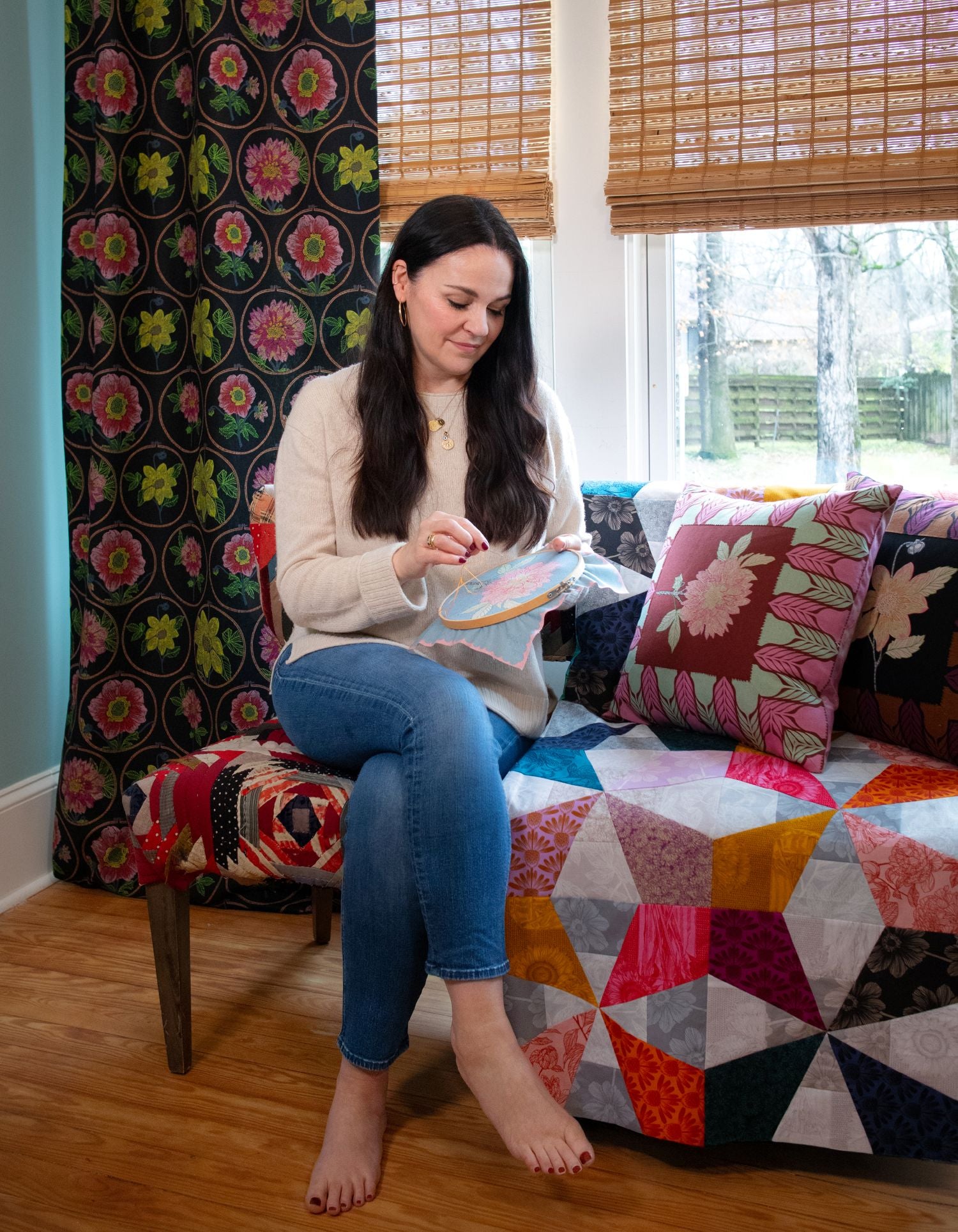 A woman is sitting on a colorful couch, sewing a piece of fabric with a needle and thread.