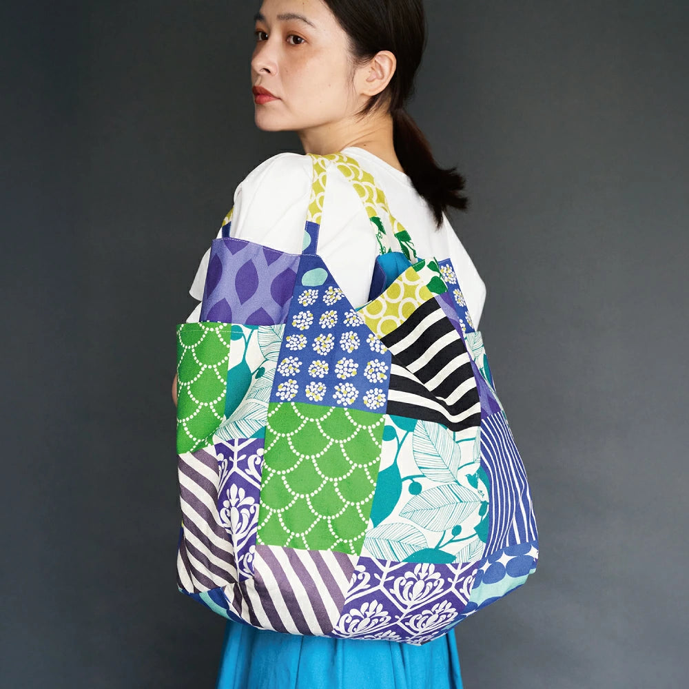 A woman wearing a white shirt and blue skirt is carrying a colorful tote bag with a pattern of various colors and designs.