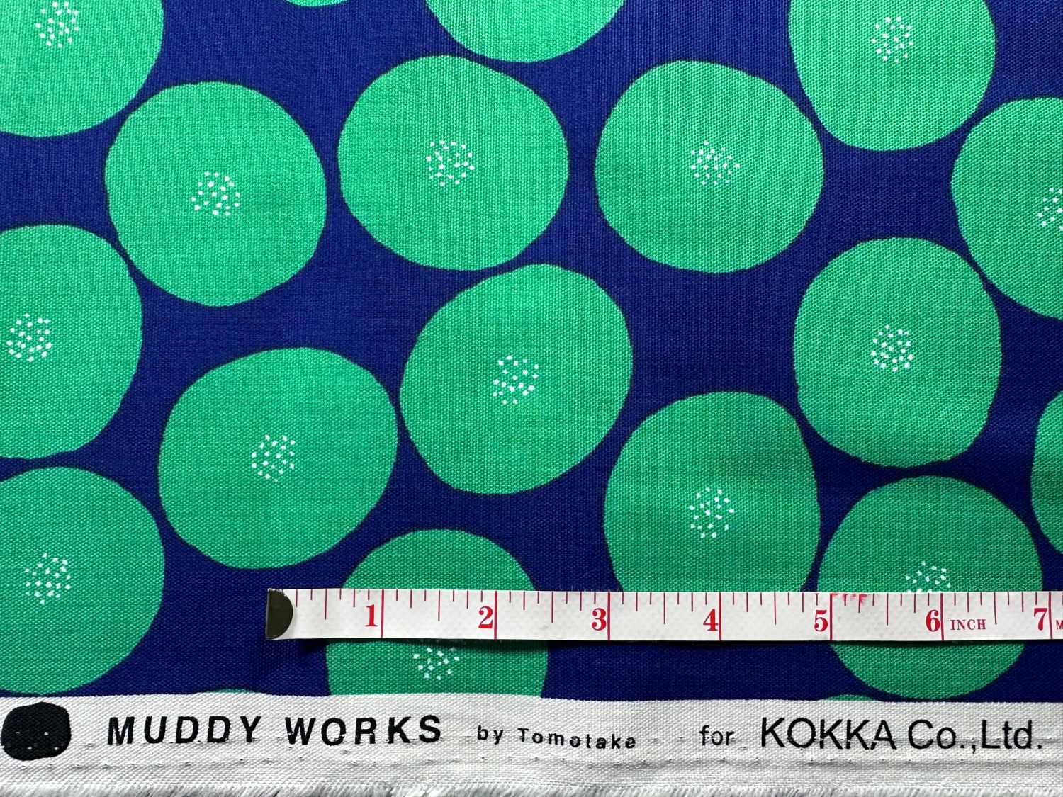 a fabric with a repeating pattern of green circles on a dark blue background. A ruler is placed in front of the fabric, indicating the size of the pattern.