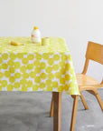 A yellow and white tablecloth with a pattern of yellow circles is spread out on a wooden table, accompanied by a bottle of lotion and a small yellow cup. A wooden chair is positioned next to the table.