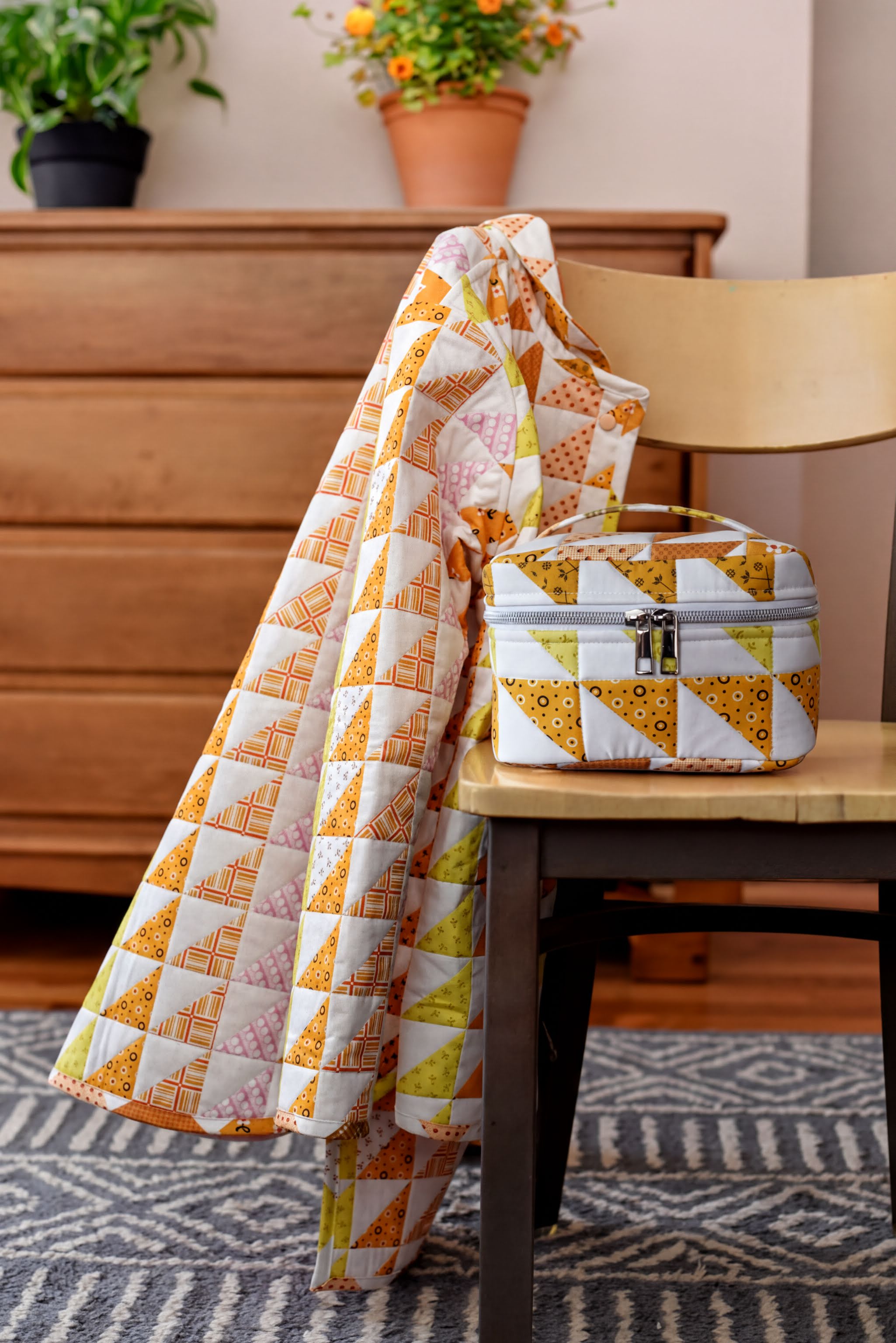 a wooden chair with a colorful quilt draped over it, a small white and yellow bag, and a potted plant in the background.