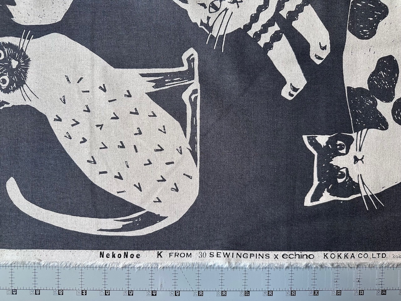 a close-up view of a fabric with a black and white cat design printed on it. The cat appears to be sitting on a surface, and there is a ruler visible in the bottom left corner of the image.