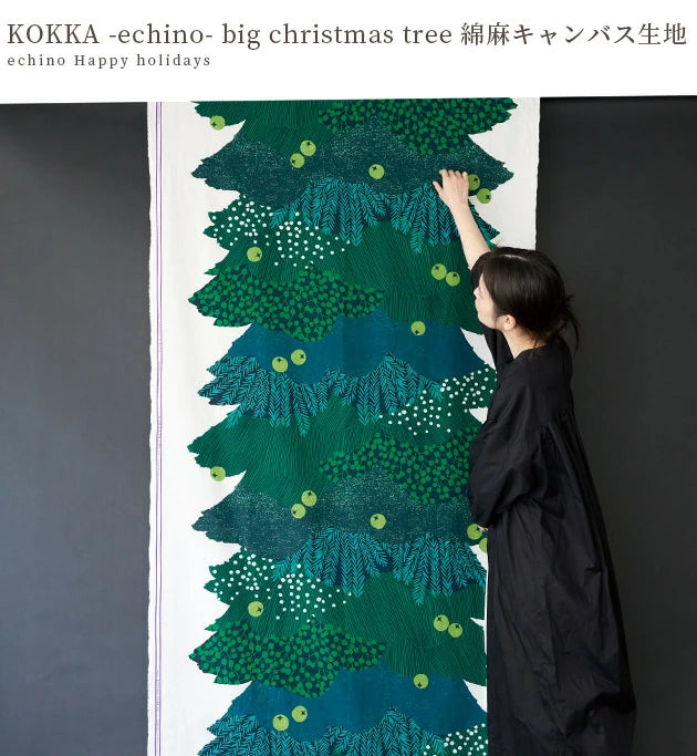 A woman in a black dress is reaching up to touch a large, colorful Christmas tree printed on a canvas.