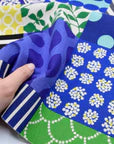 A hand is holding a fabric with a vibrant, colorful pattern of various shapes and designs, including polka dots, stripes, and floral motifs.