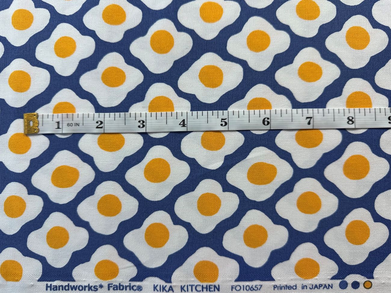 a fabric with a repeating pattern of white and orange egg shapes, with a ruler placed over the fabric to indicate the size.