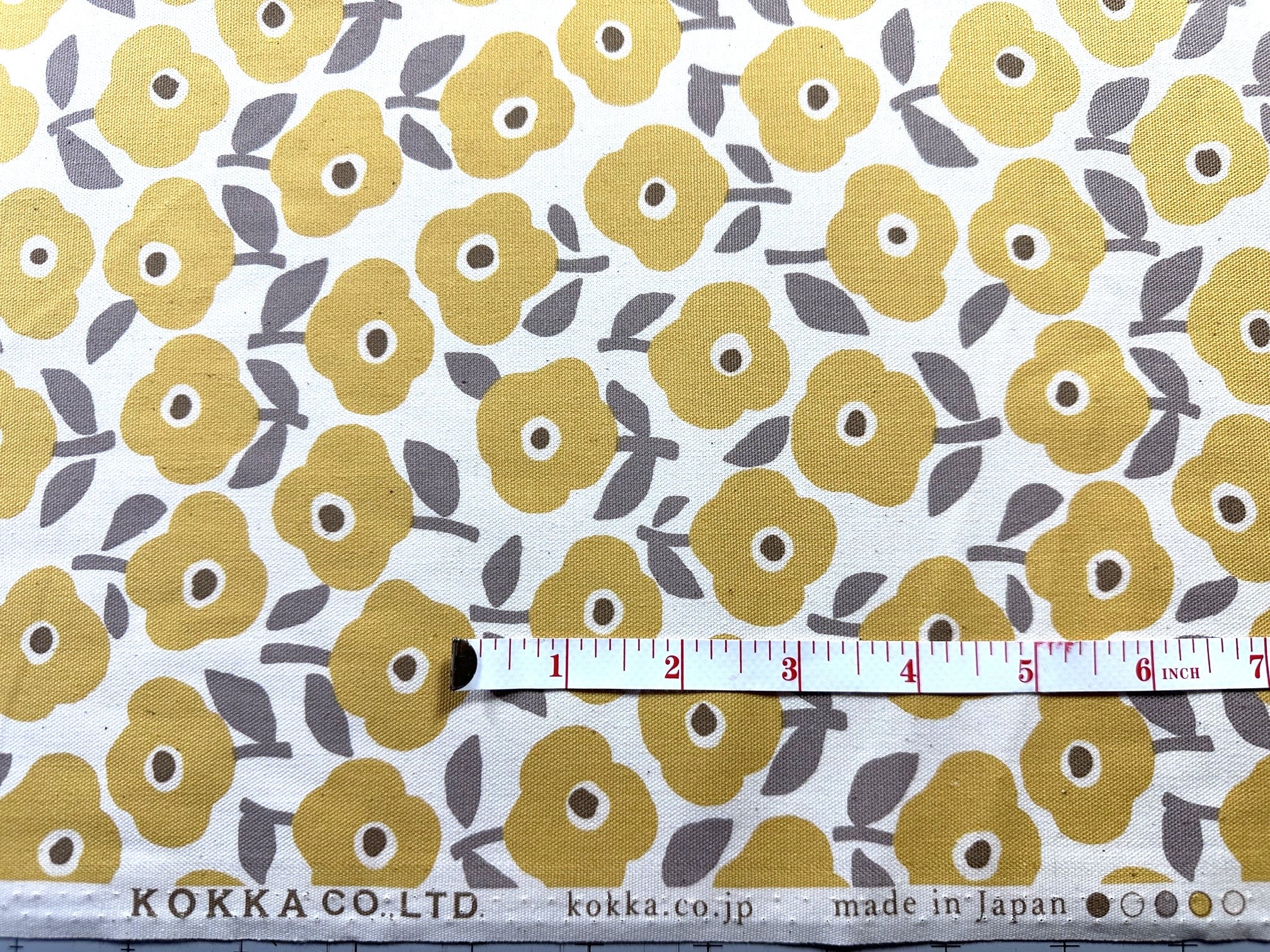 a fabric with a repeating pattern of yellow flowers on a white background. A ruler is placed next to the fabric, indicating the size of the fabric.