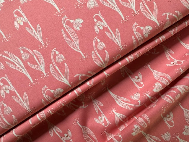 a close-up view of a fabric with a repeating pattern of white flowers or leaves against a pink background.