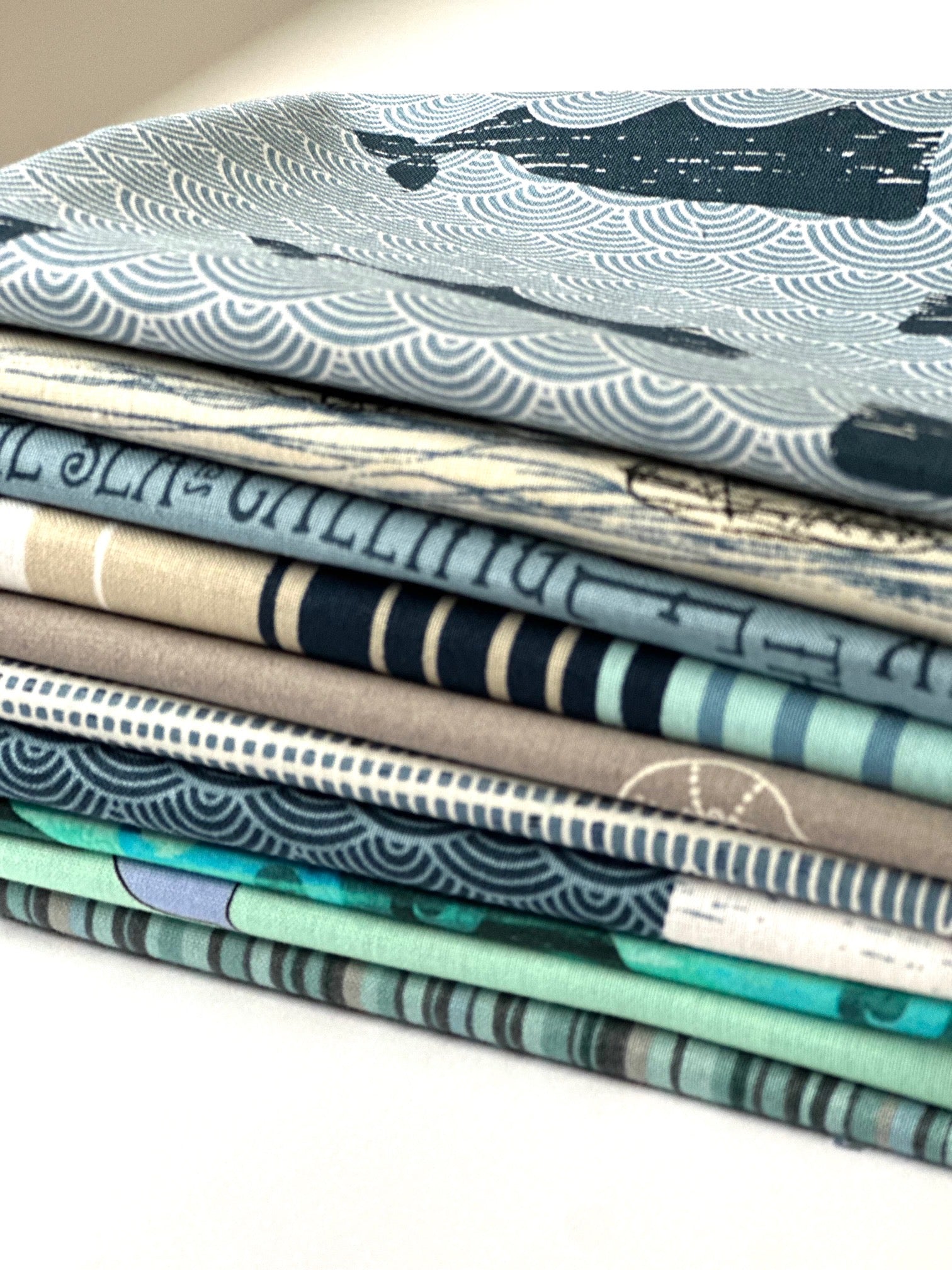 A stack of various fabric swatches in shades of blue, gray, and beige, with some featuring patterns like waves and fish.