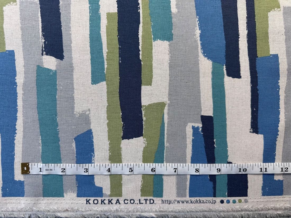 a fabric with a striped pattern in shades of blue, green, and gray. A ruler is placed in front of the fabric, indicating the size of the fabric.