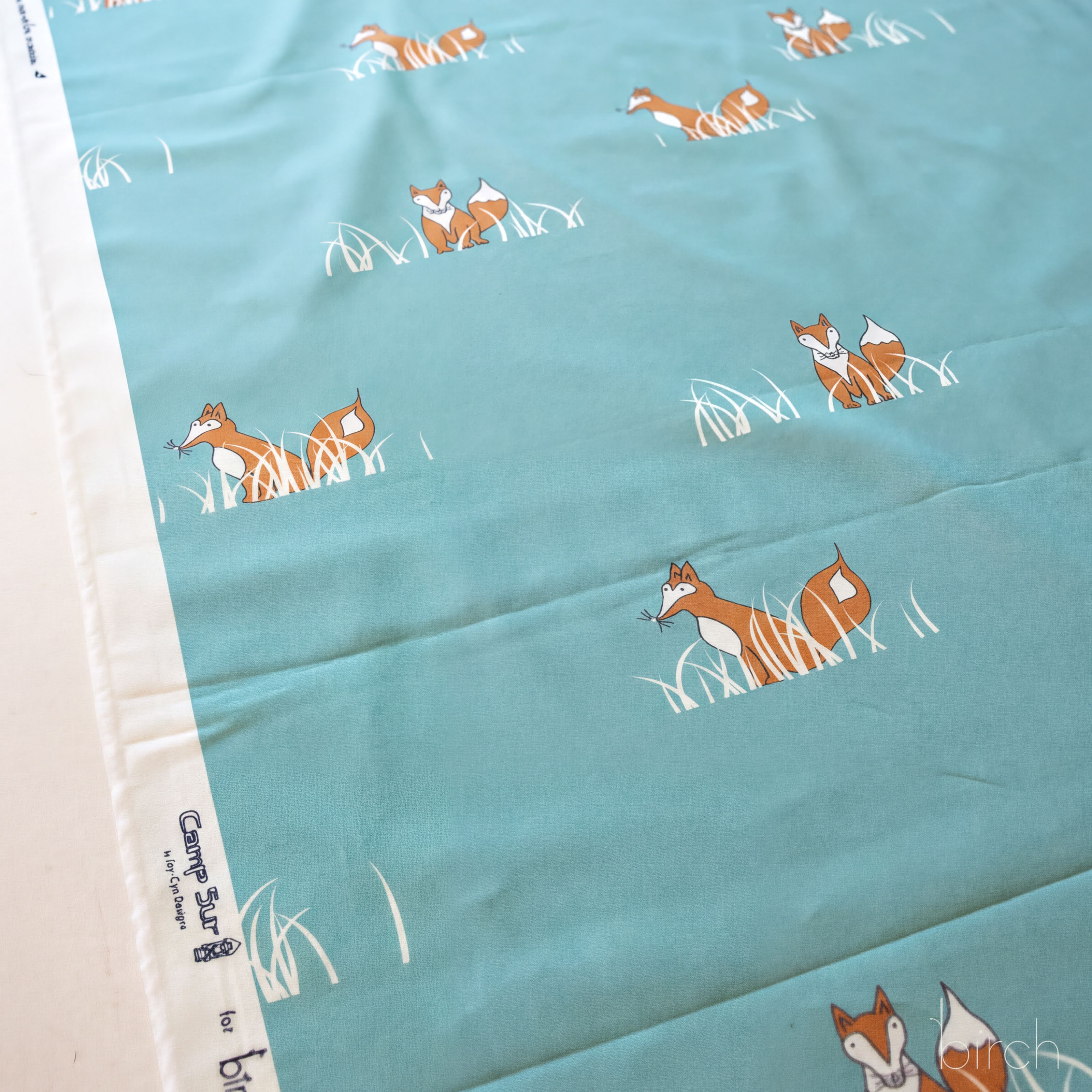 a fabric with a repeating pattern of cartoon-like foxes in a grassy field.