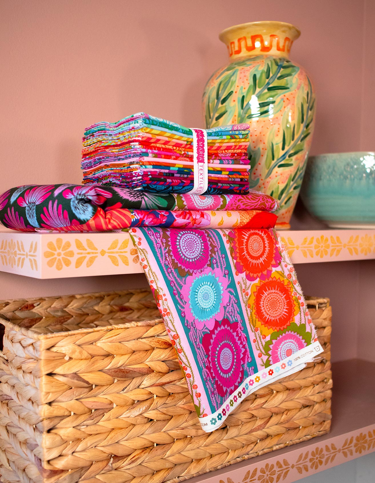 a collection of colorful fabric and decorative items, including a vase with a floral design, arranged on a shelf.