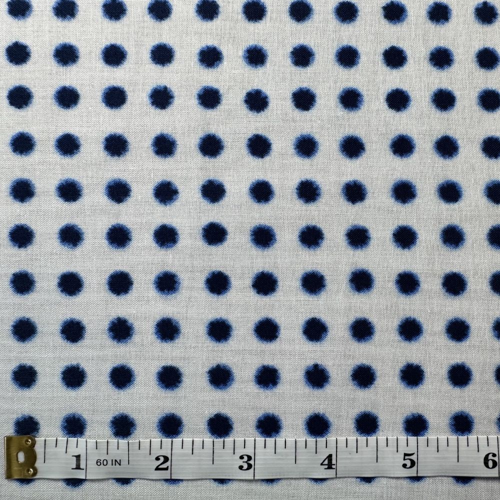 a close-up view of a fabric with a pattern of blue dots on a white background. A ruler is placed next to the fabric, indicating the size of the fabric.