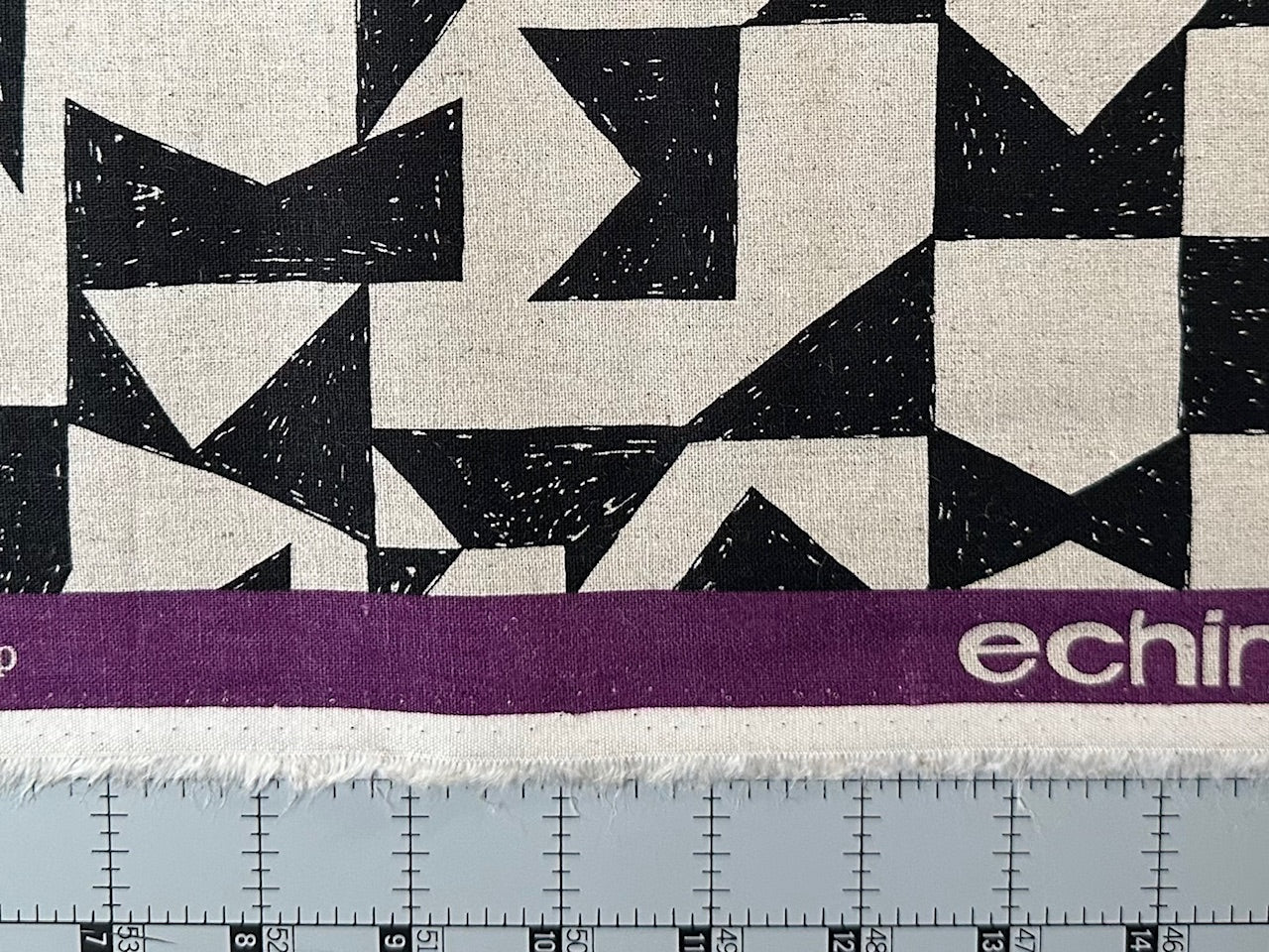 a close-up view of a fabric with a geometric pattern of black and white triangles. The fabric is placed on a purple measuring tape, which is marked with the word "echino" in white text.