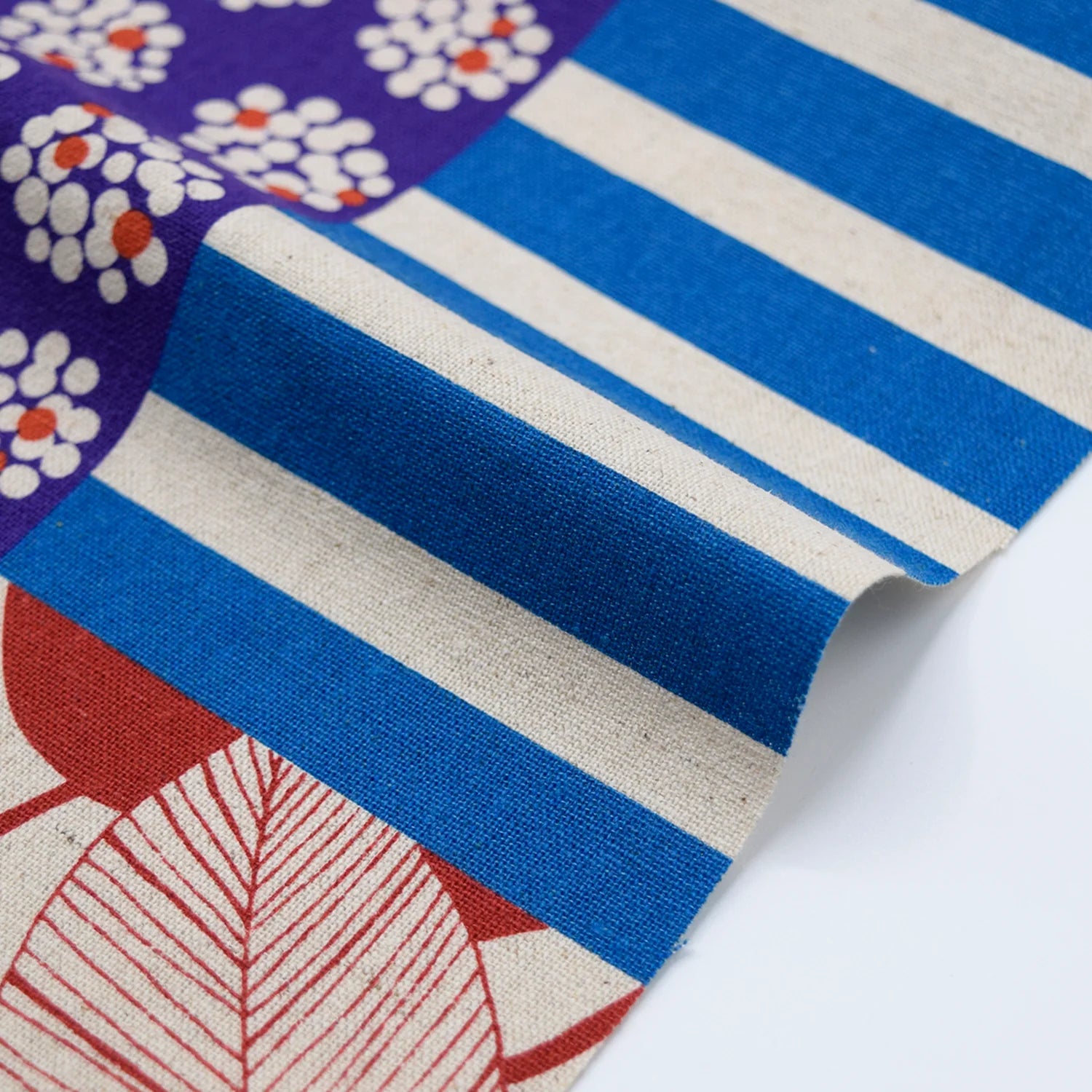 The image is a close-up view of a fabric with a pattern of blue and white stripes, along with a red leaf design.