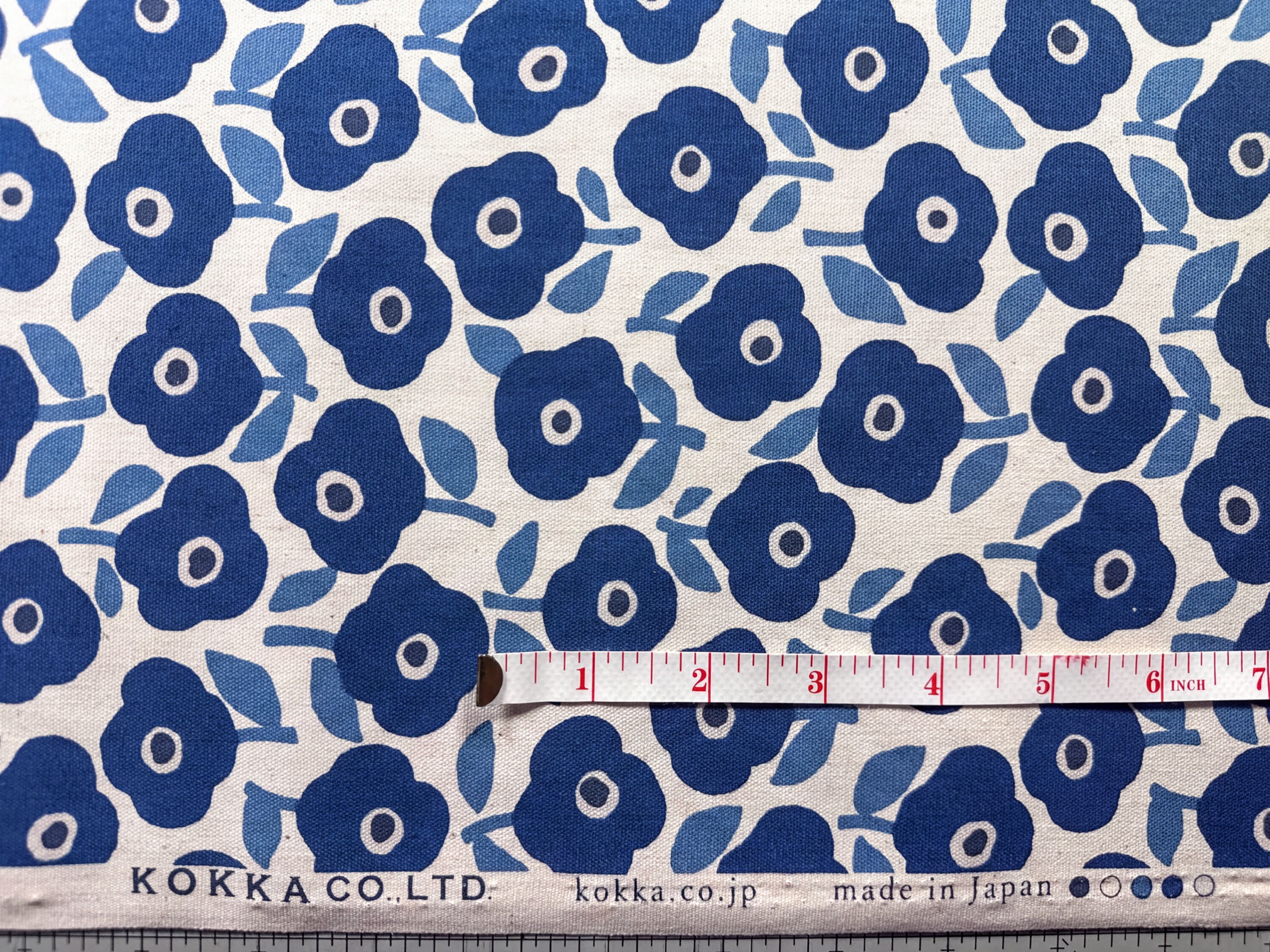 a fabric with a repeating pattern of blue flowers on a white background. A ruler is placed next to the fabric, indicating the size of the fabric.