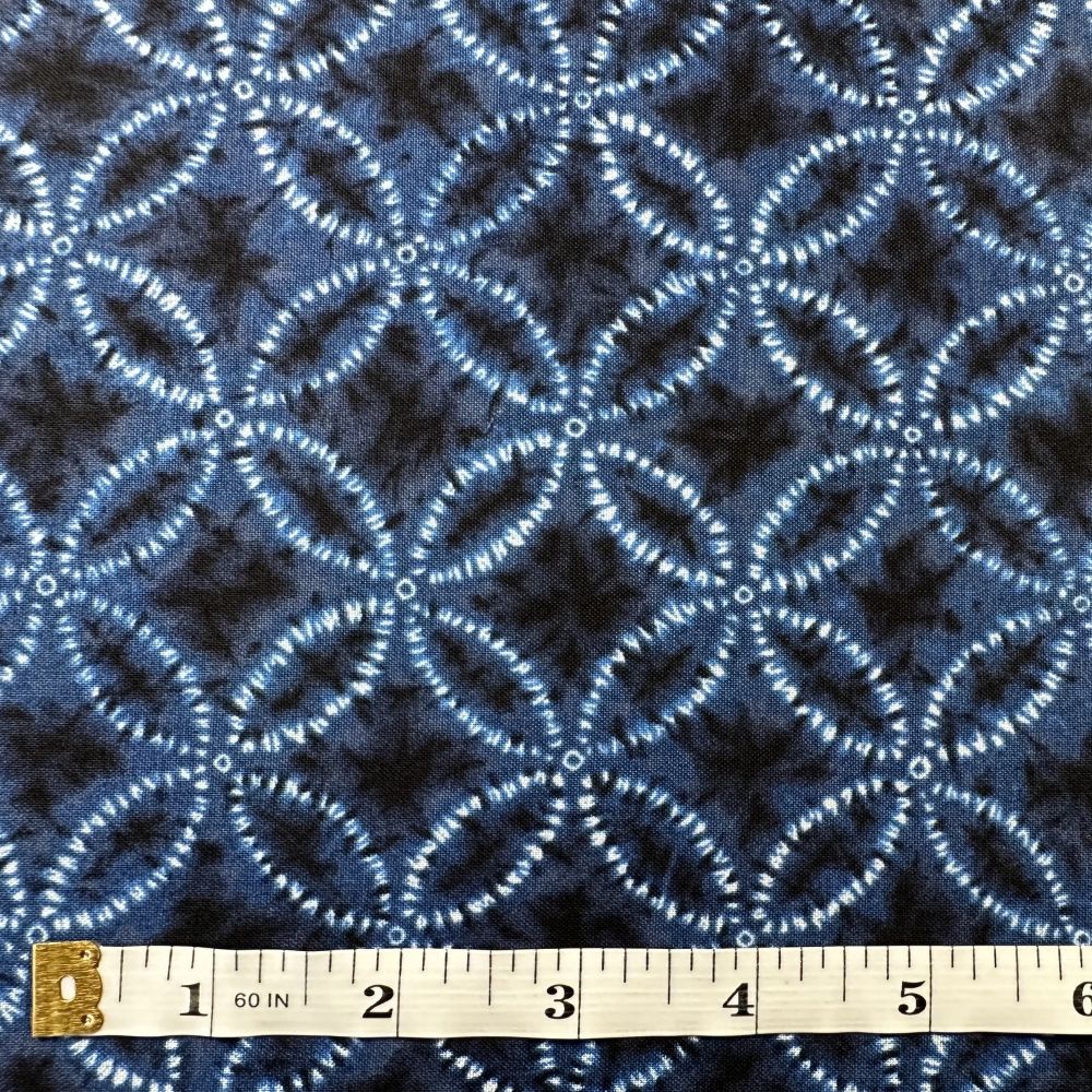 a close-up view of a fabric with a repeating pattern of blue and white circles or ovals, creating a visually striking and intricate design. The fabric appears to be a type of textile, possibly a piece of clothing or a decorative item. A ruler is placed in front of the fabric, indicating its size and providing a reference for the viewer.