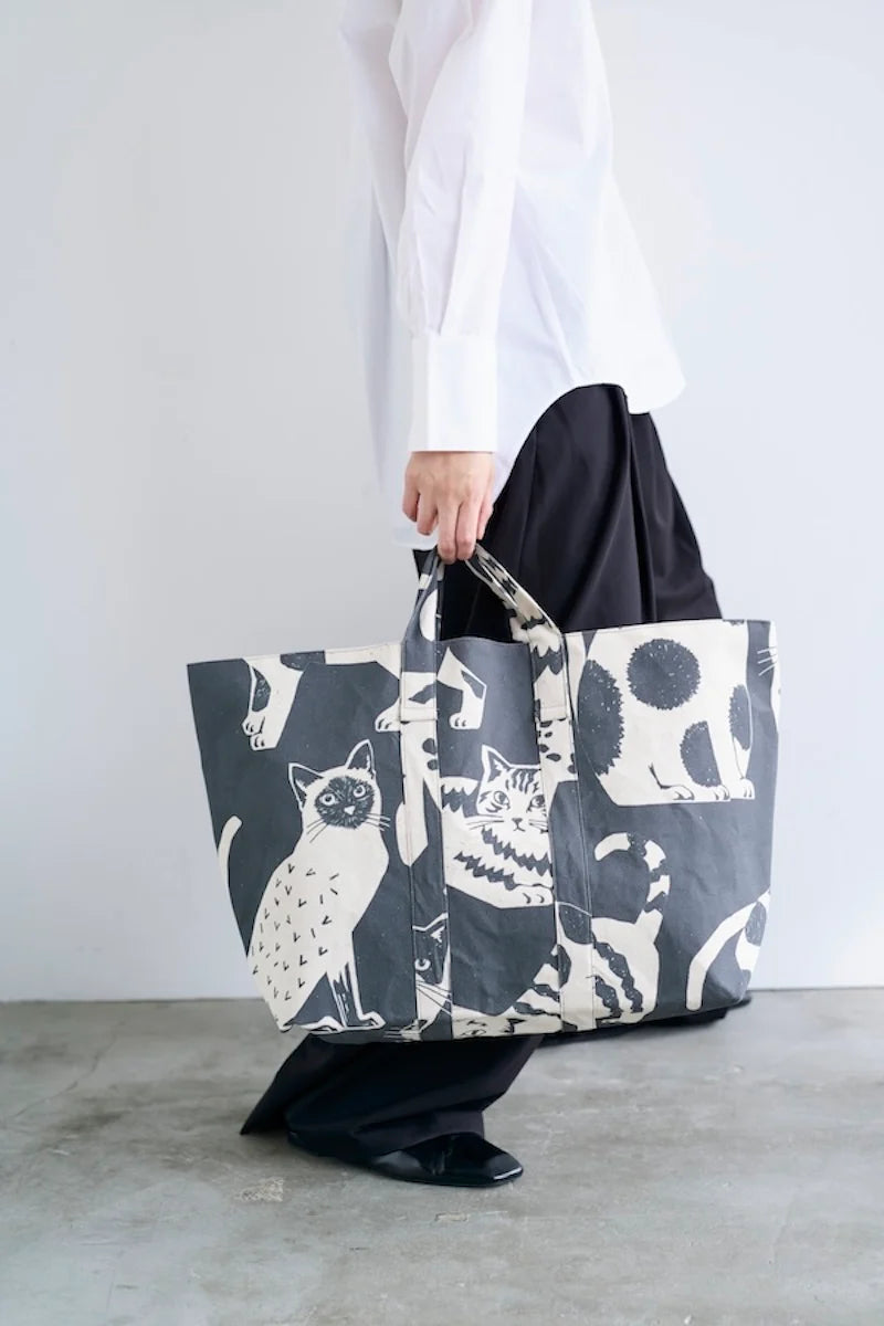 A person is holding a large tote bag with a cat print design.