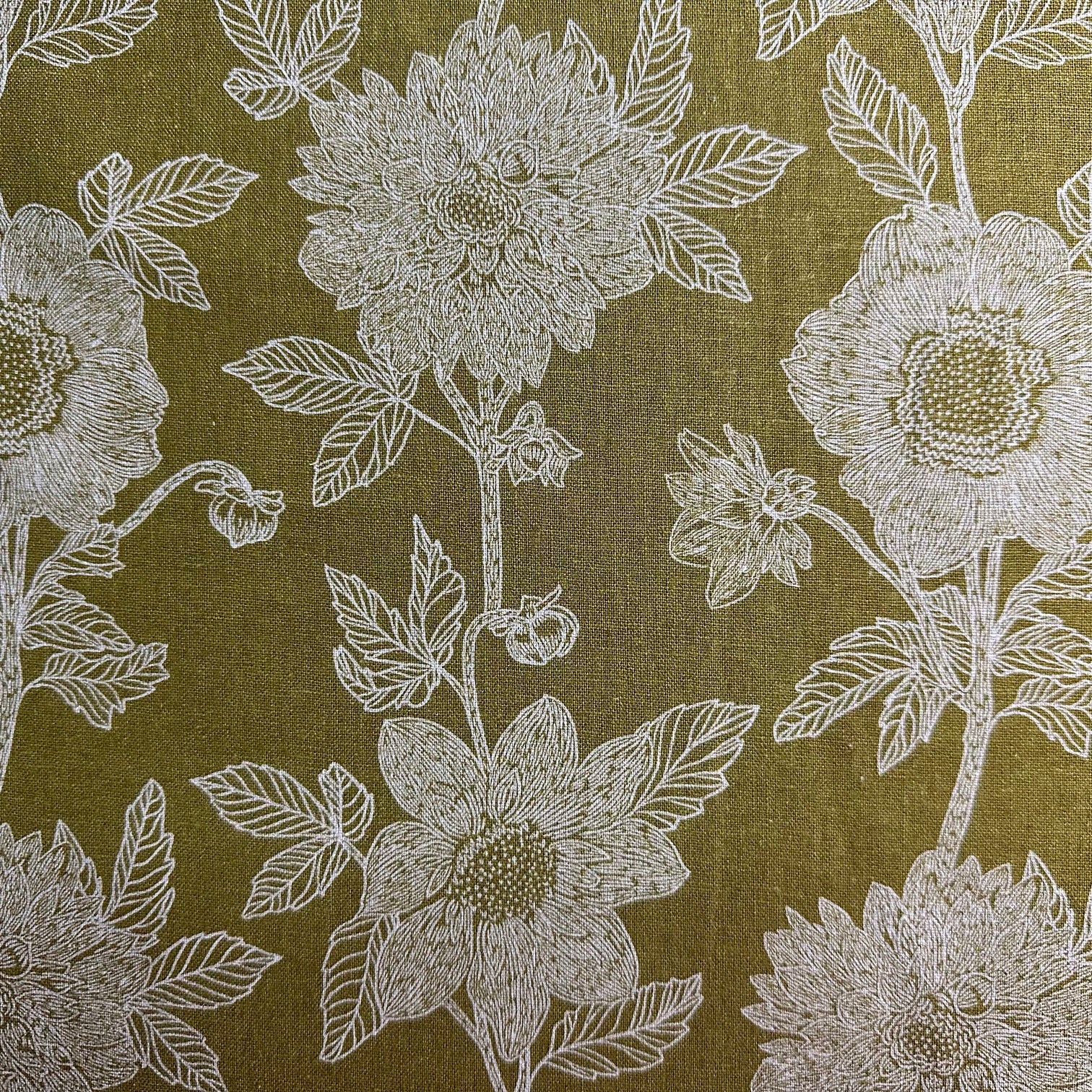 a close-up view of a fabric with a repeating floral pattern. The pattern consists of white flowers with green leaves, creating a visually appealing and intricate design. The fabric appears to be a type of wallpaper or textile, with a textured and textured appearance.