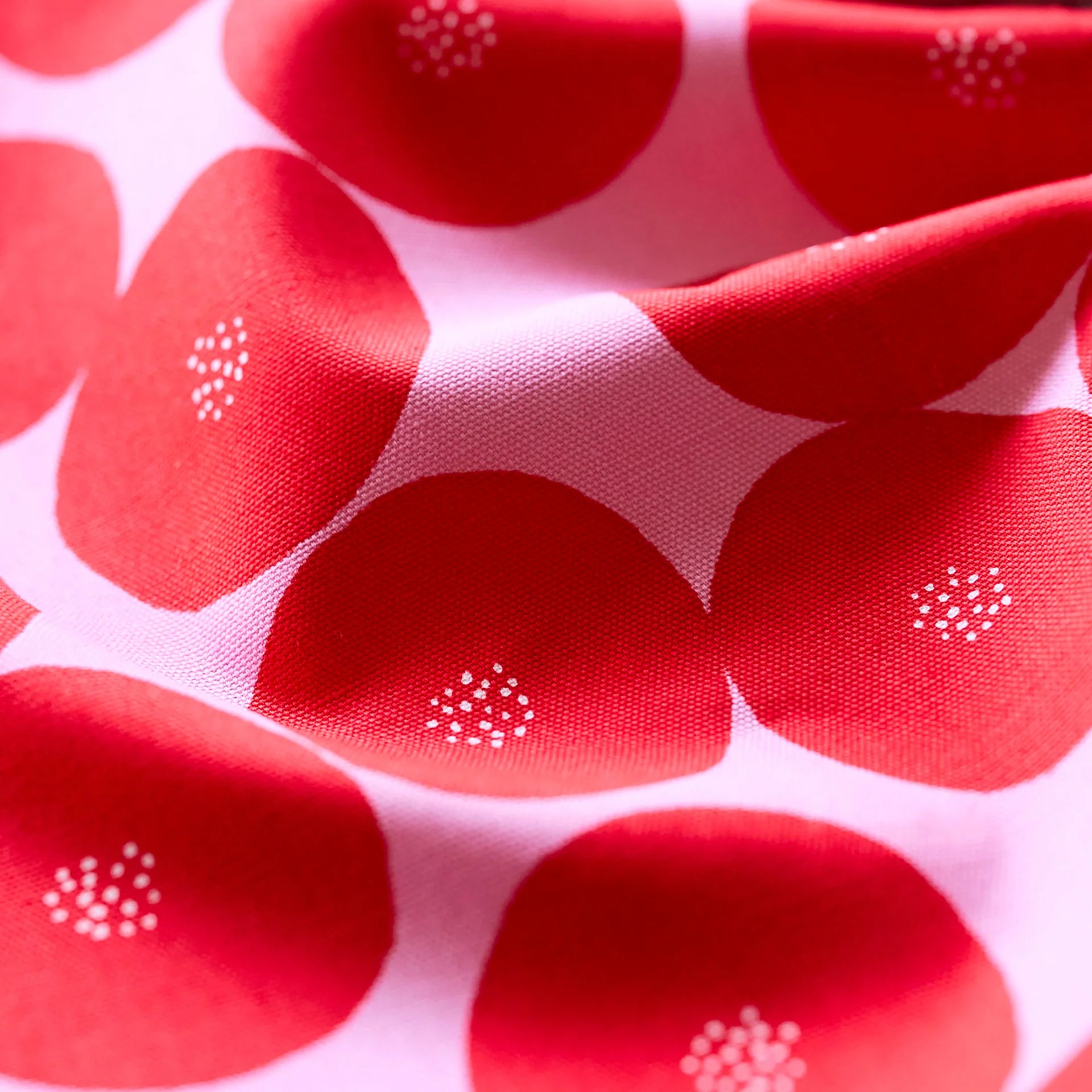 a close-up view of a fabric with a repeating pattern of red flowers with white spots. The fabric appears to be soft and has a slightly wrinkled texture.