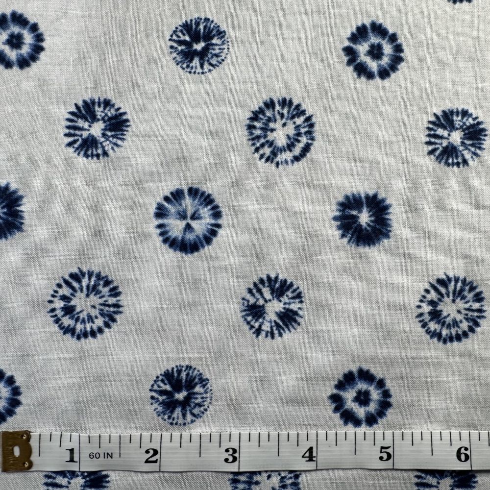 a fabric with a repeating pattern of blue and white circles or dots, creating a tie-dye effect. The fabric appears to be a light-colored material, possibly cotton or linen, with a white background. A ruler is placed in front of the fabric, likely for measuring purposes.