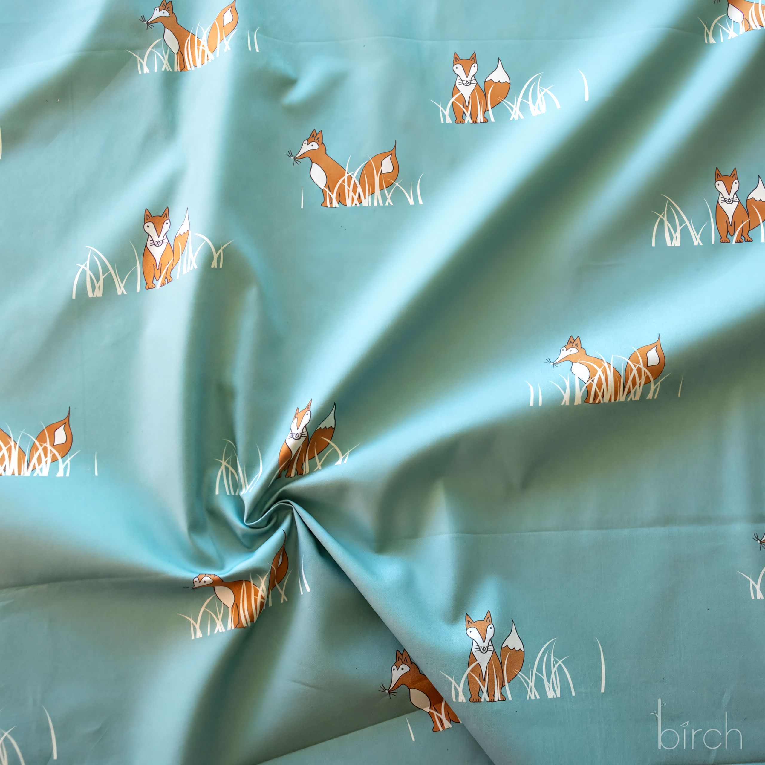a fabric with a repeating pattern of orange foxes sitting in the grass.
