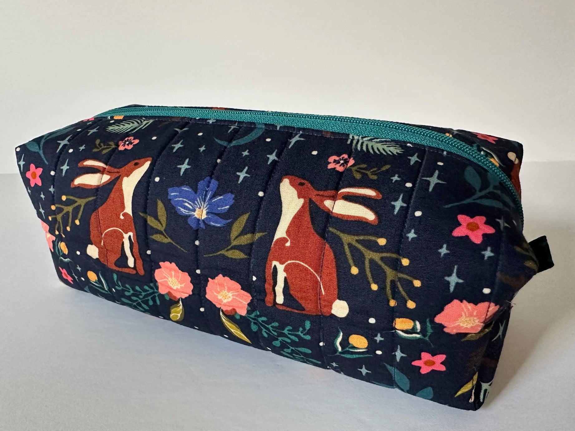 A colorful makeup bag with a floral pattern and illustrations of rabbits.