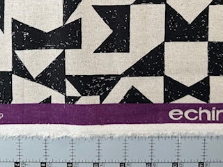 a close-up view of a fabric with a geometric pattern in black and white, with a purple border. The fabric appears to be a piece of clothing or textile, and there is a ruler visible in the bottom right corner of the image.