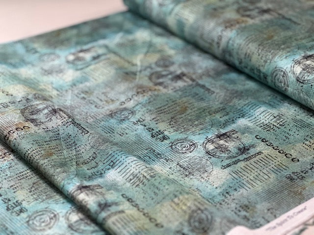 a close-up view of a fabric with a repeating pattern of black and white text and circular designs. The fabric appears to be a blend of blue and green colors, with the text and designs appearing to be printed on it.