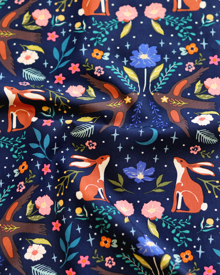 a vibrant and colorful fabric with a repeating pattern of rabbits, flowers, leaves, and stars. The pattern is a mix of various colors and shapes, creating a visually striking and whimsical design.