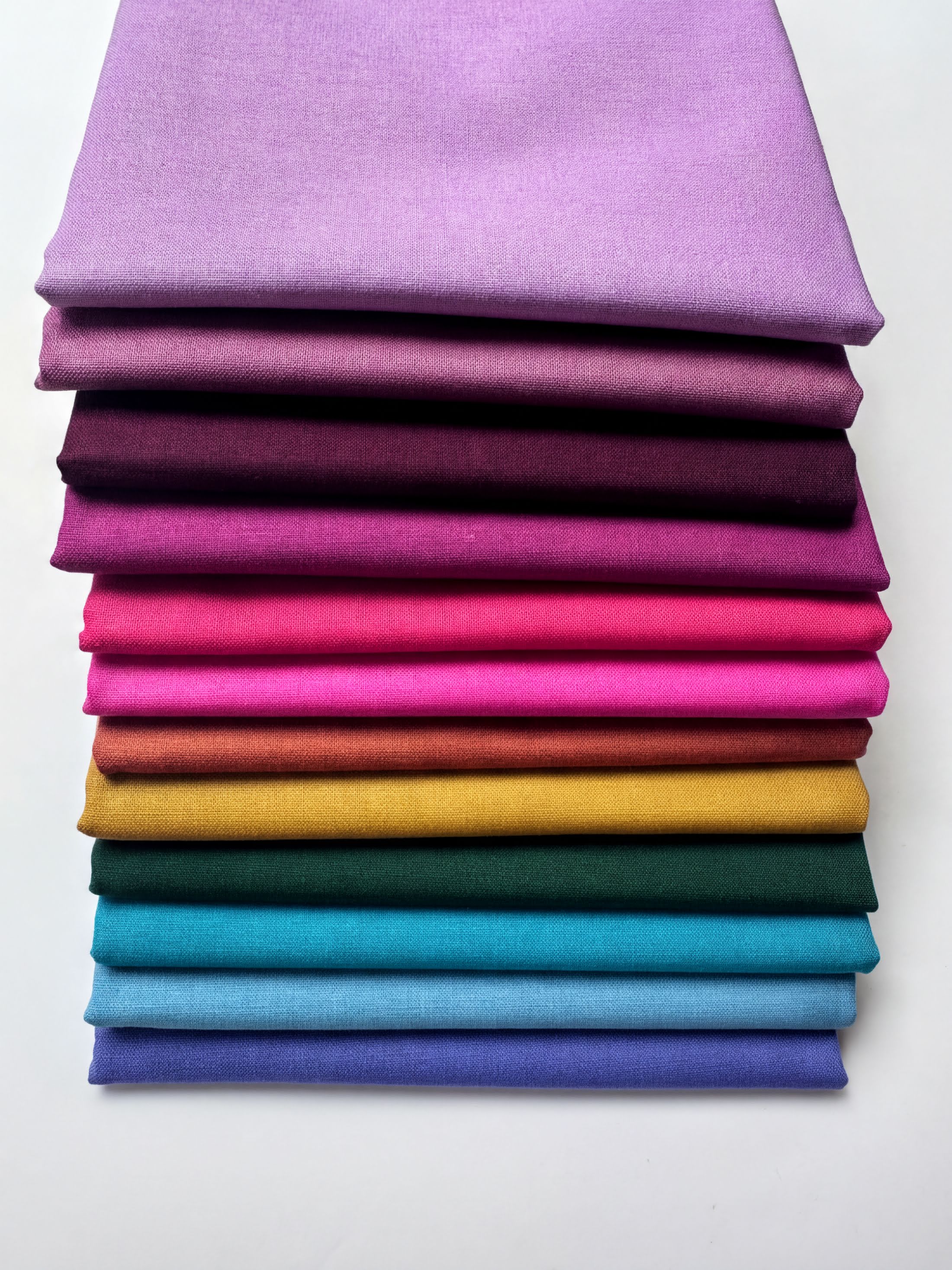A stack of colorful fabric swatches in various shades of purple, pink, orange, yellow, green, blue, and purple.