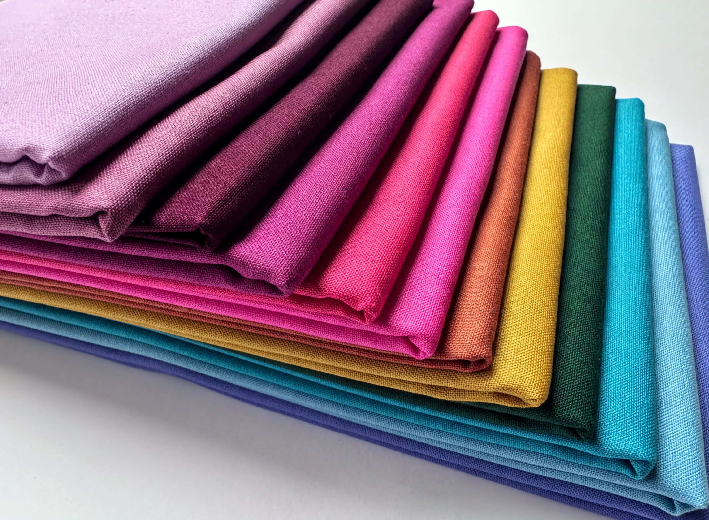 A stack of colorful fabric swatches in various shades of purple, pink, orange, yellow, green, blue, and turquoise.