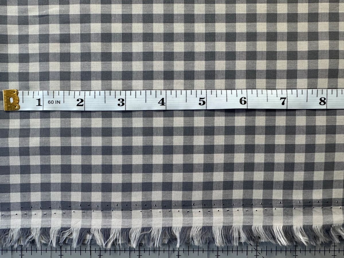 a close-up view of a fabric with a gingham pattern, featuring a ruler for scale.