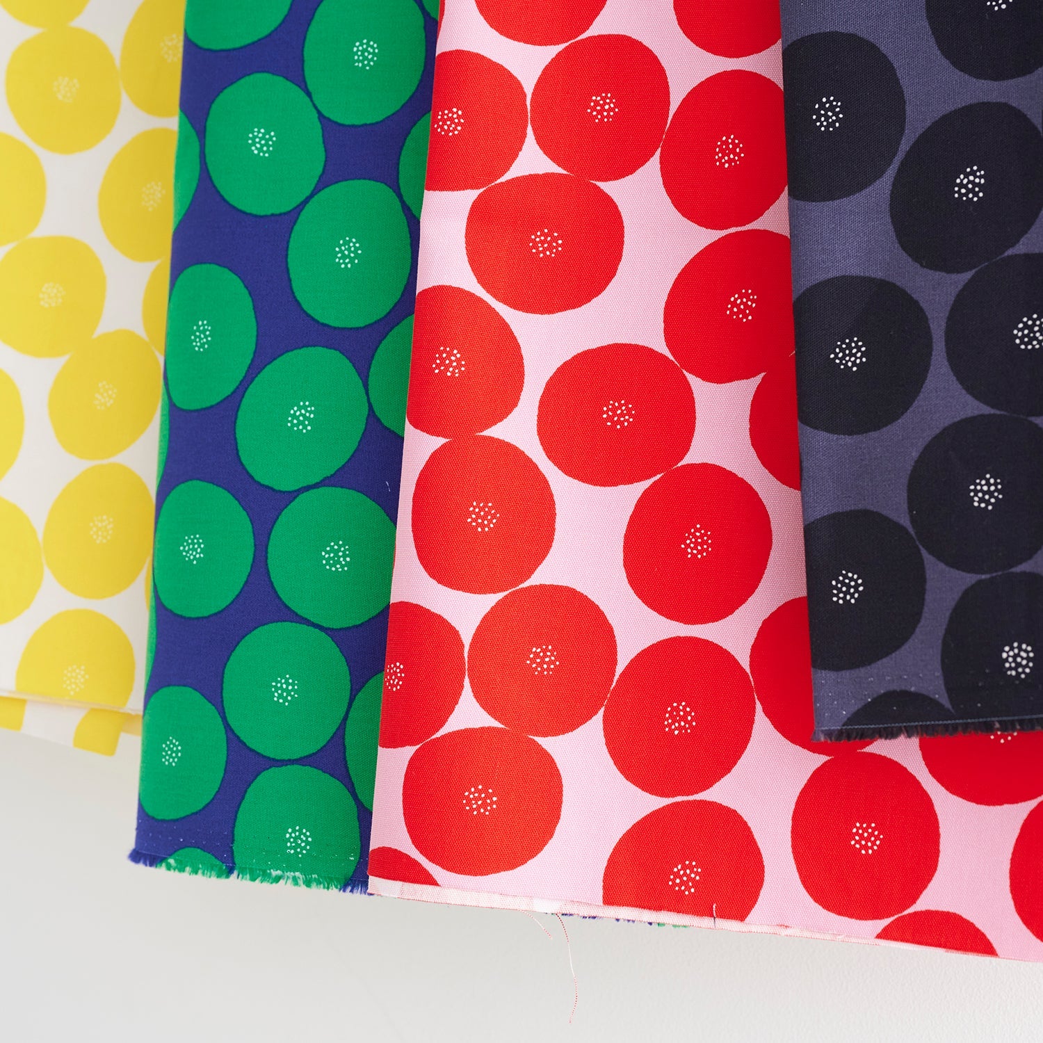 four fabric swatches with different patterns of circles, including green, red, yellow, and black circles with white dots.