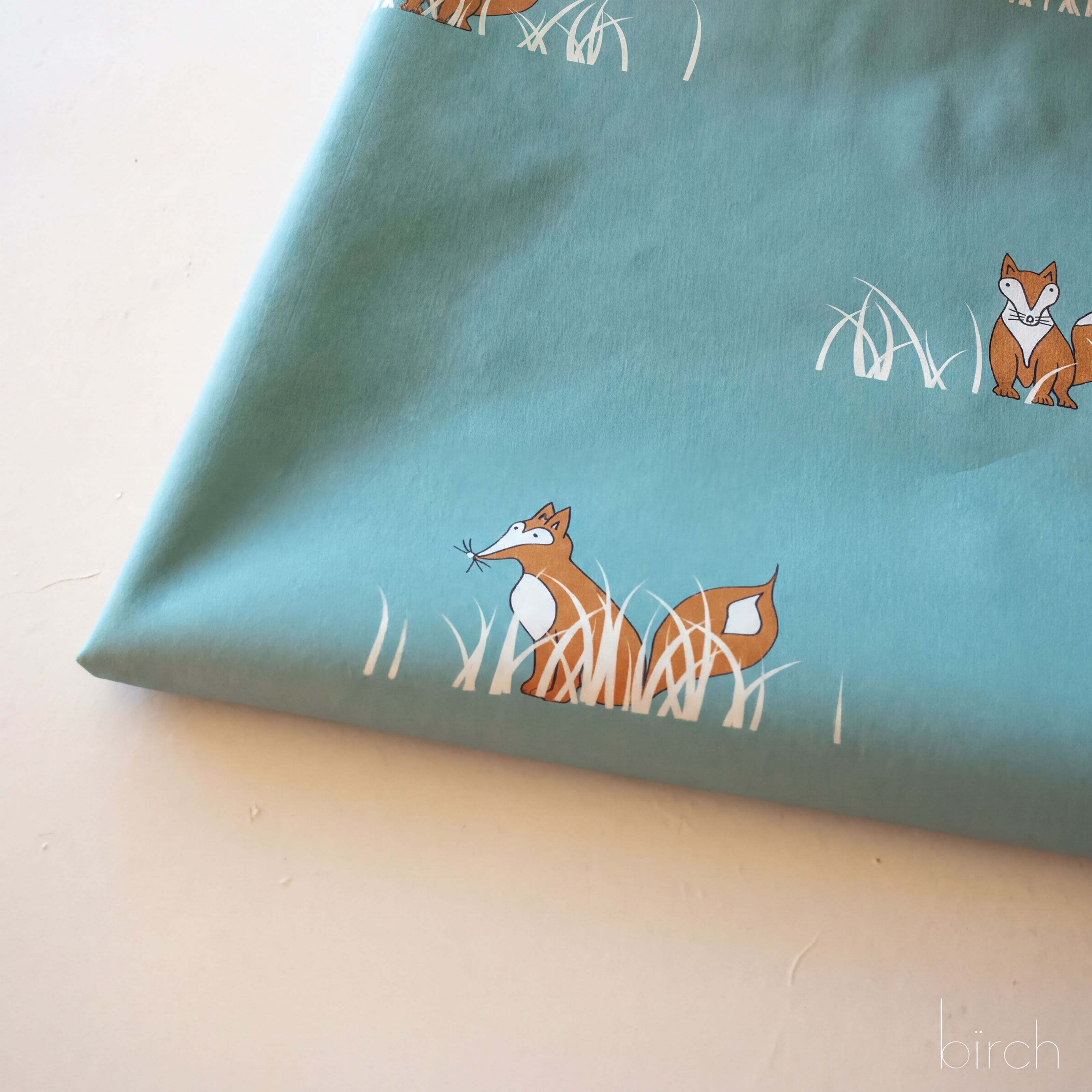 a fabric with a pattern of cartoon foxes in a grassy field.
