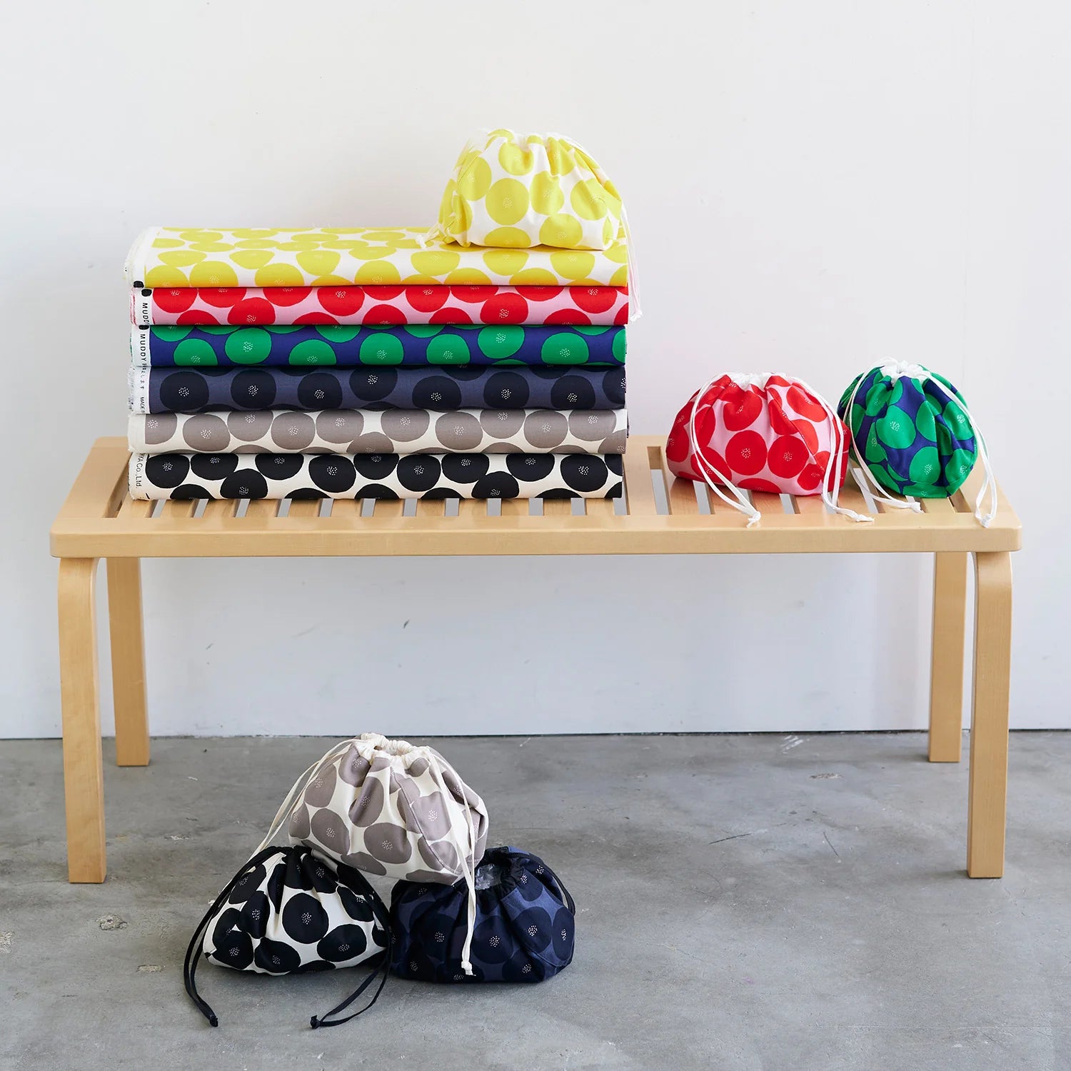A wooden bench with a stack of colorful fabric bags and drawstring bags placed on it.