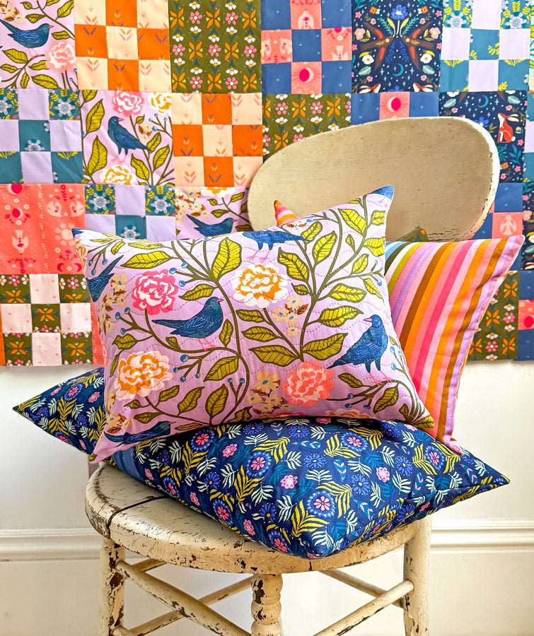 a wooden chair with colorful pillows on it, set against a backdrop of a vibrant, patterned quilt.