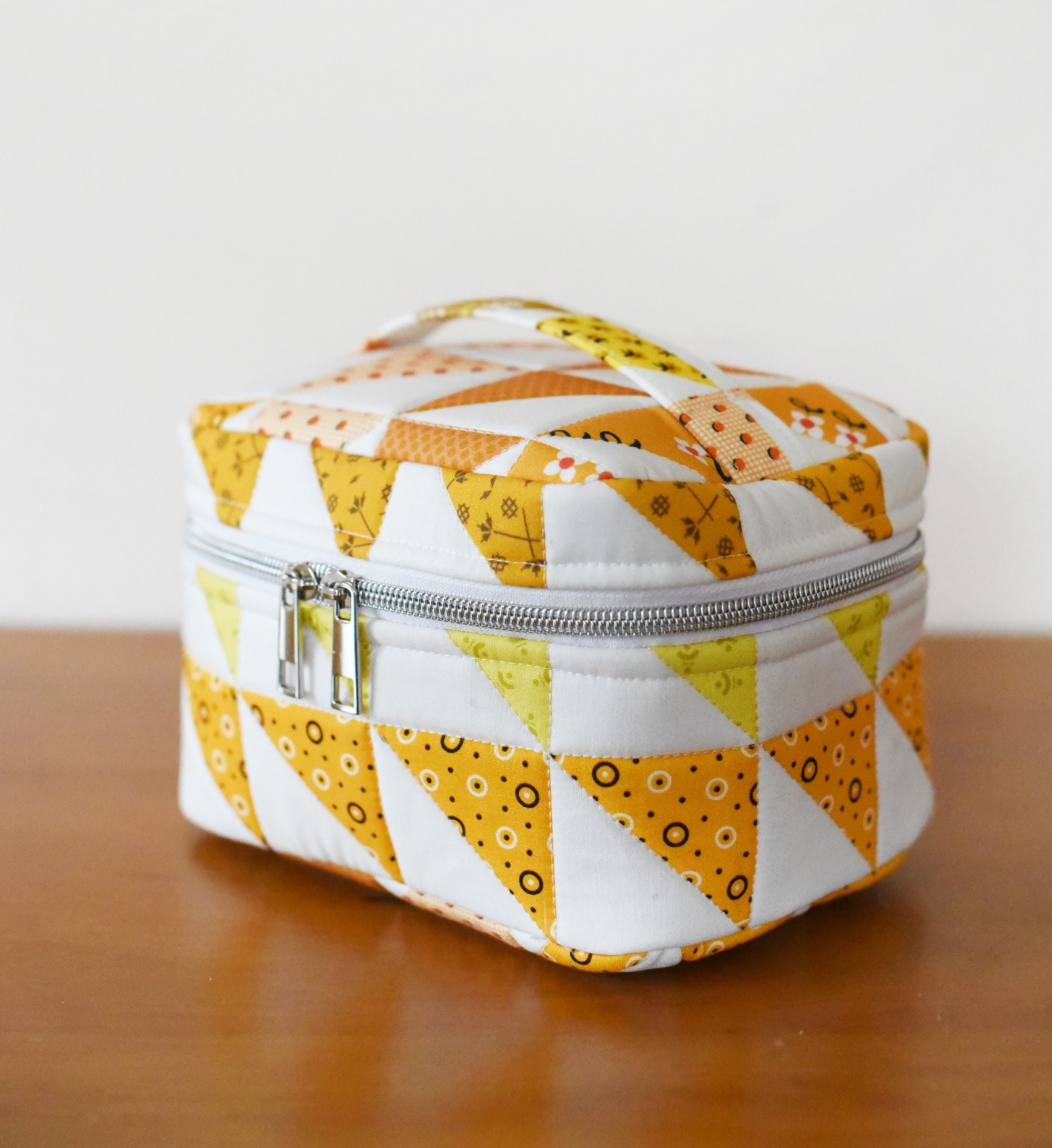 A white and yellow patterned cosmetic bag with a zipper closure, sitting on a wooden surface.