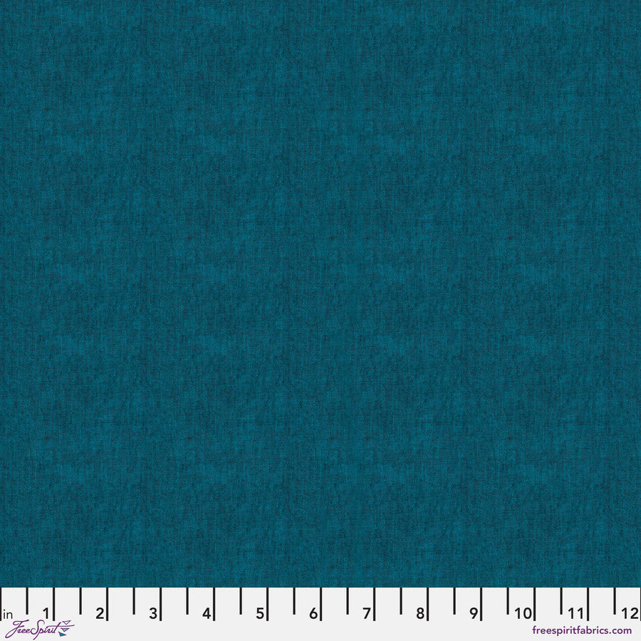 The image is a close-up of a solid teal fabric, with a ruler at the bottom providing a scale for size reference.